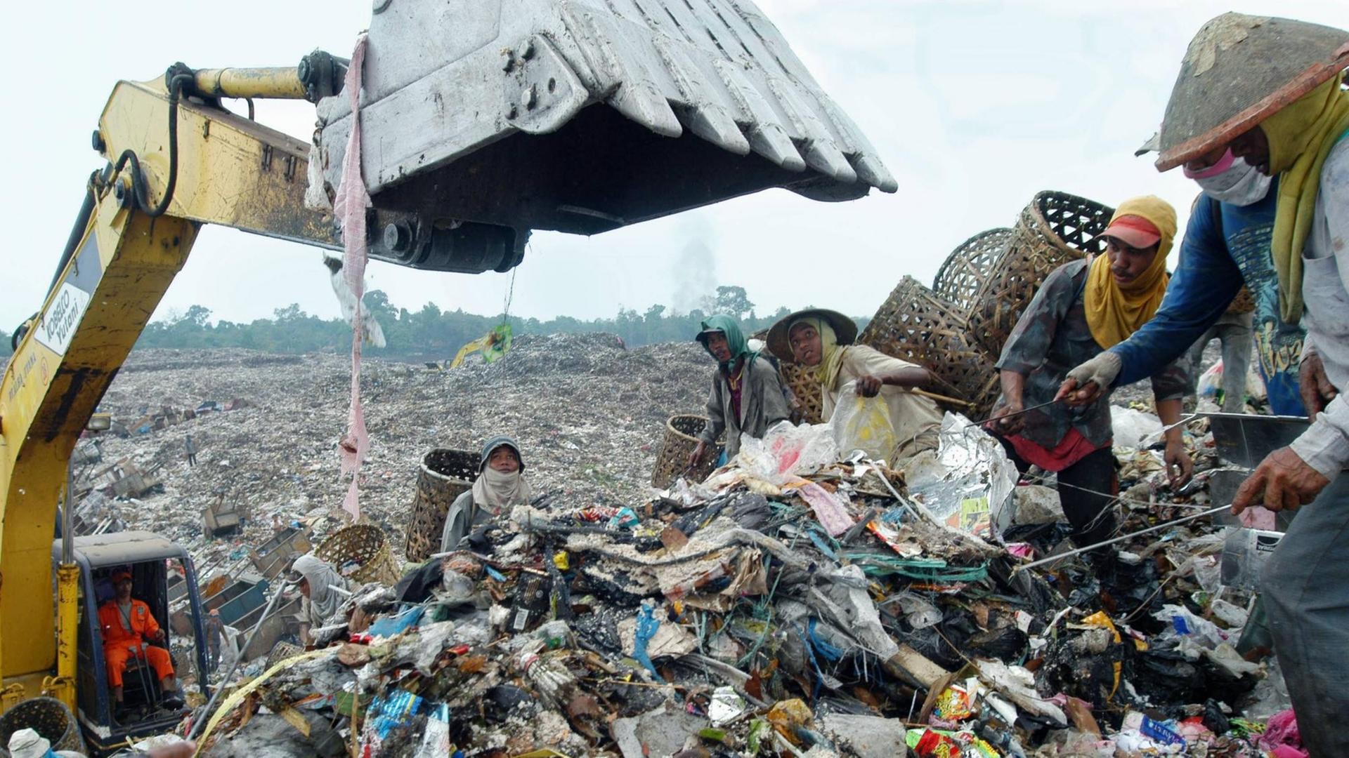 Straßenkinder stehen inmitten von Abfällen neben einem Bagger auf einer Müllhalde in Malaysia, Aufnahme geschätzt, ca. 2012