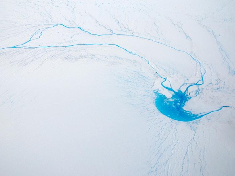 Das Foto zeigt einen einen Fluss, der im Eis eines Gletschers auf Grönland verschwindet.