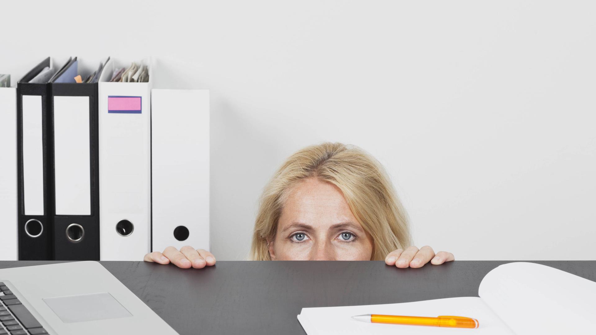 Eien Frau versteckt sich hinter einem Schreibtisch im Büro. Eien Frau versteckt sich hinter einem Schreibtisch im Büro.