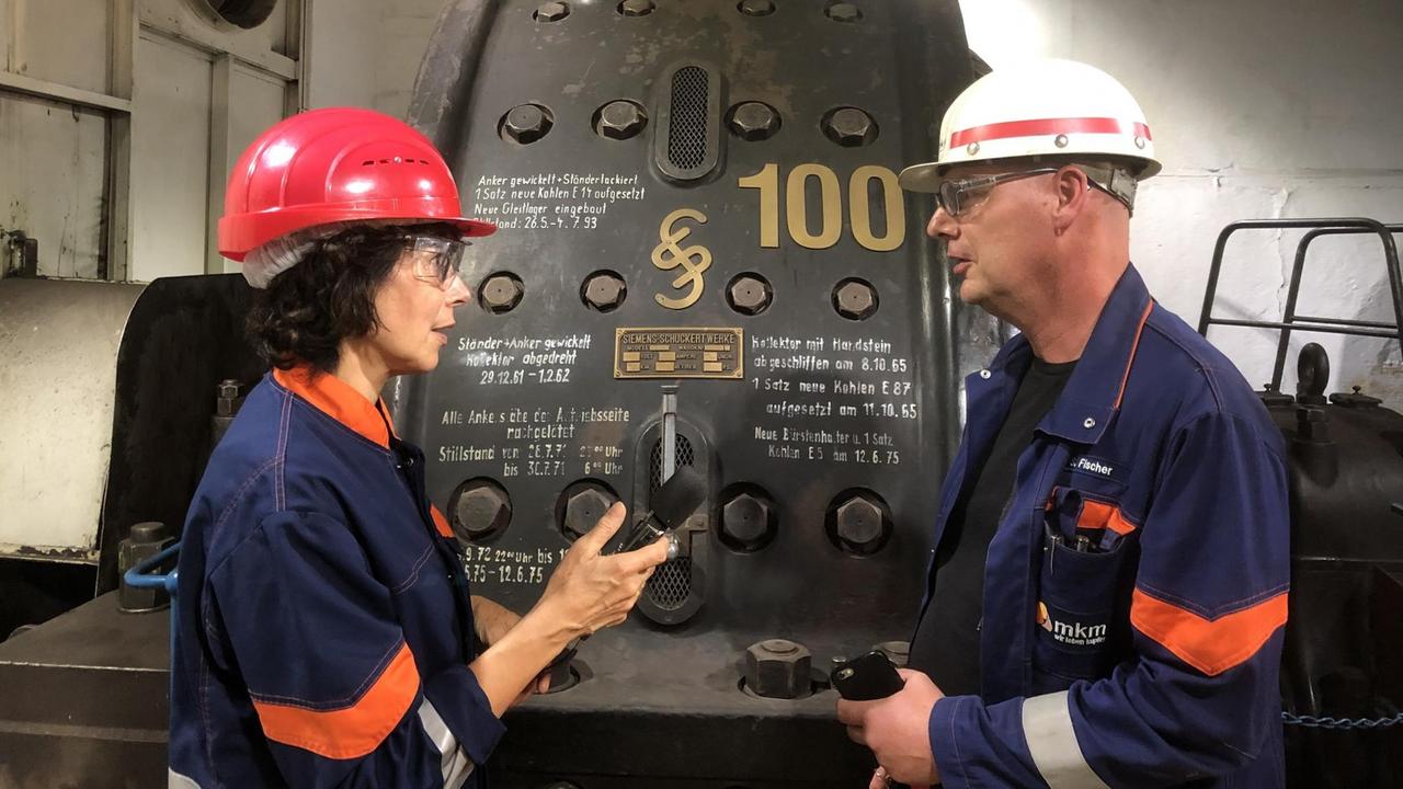 Sabine Adler spricht mit einem Angestellten vor den historischen Maschinen. Sabine Adler spricht mit einem Angestellten vor den historischen Maschinen.