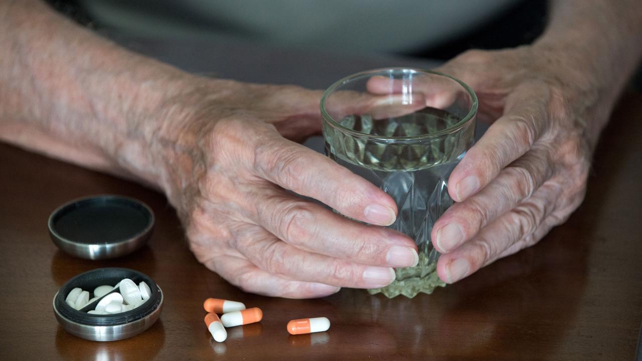 Ein älterer Mensch mit einem Wasserglas in der Hand und bereit gelegten Tabletten Ein älterer Mensch mit einem Wasserglas in der Hand und bereit gelegten Tabletten