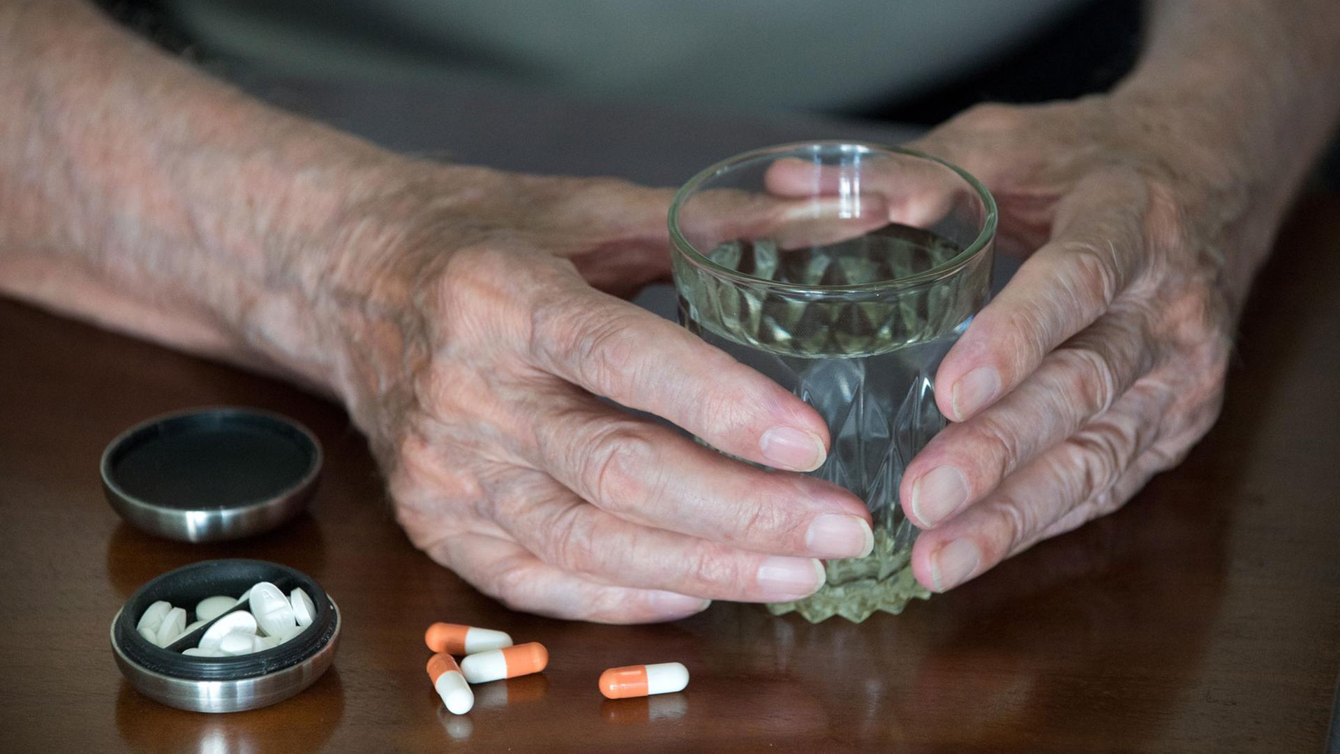 Ein älterer Mensch mit einem Wasserglas in der Hand und bereit gelegten Tabletten Ein älterer Mensch mit einem Wasserglas in der Hand und bereit gelegten Tabletten