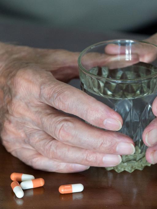 Ein älterer Mensch mit einem Wasserglas in der Hand und bereit gelegten Tabletten