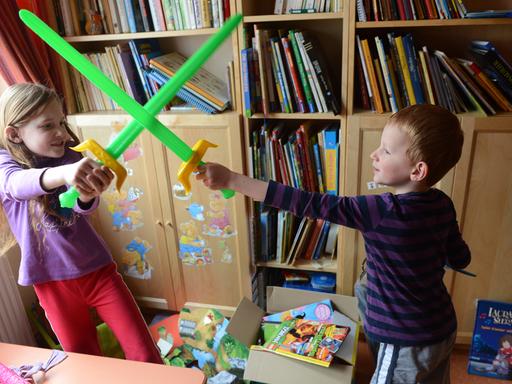 Ein achtjähriges Mädchen und ein fünfjähriger Junge "kämpfen" in ihrem Kinderzimmer mit Plastikschwertern gegeneinander.