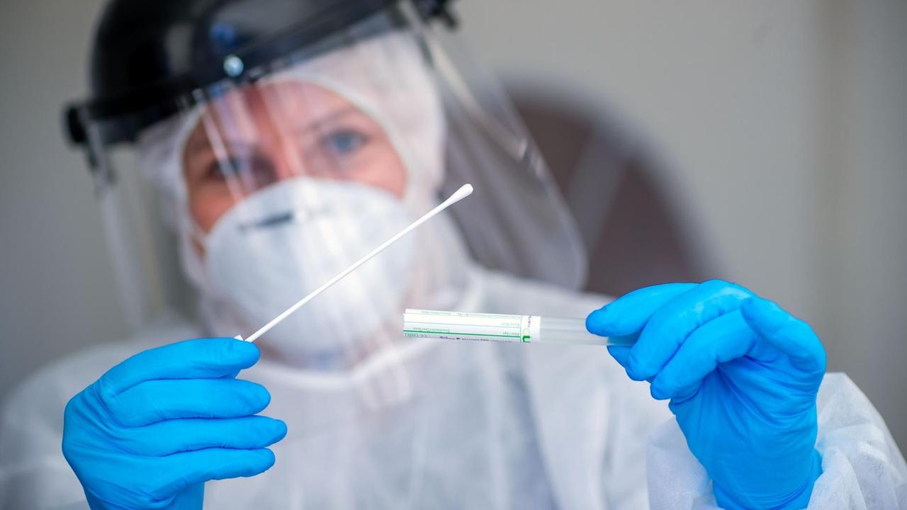 Mit einem Abstrichstäbchen nimmt eine Ärztin von einem Patienten in einem Auto eine Probe im Testzentrum für Corona-Verdachtsfälle. Mit einem Abstrichstäbchen nimmt eine Ärztin von einem Patienten in einem Auto eine Probe im Testzentrum für Corona-Verdachtsfälle.