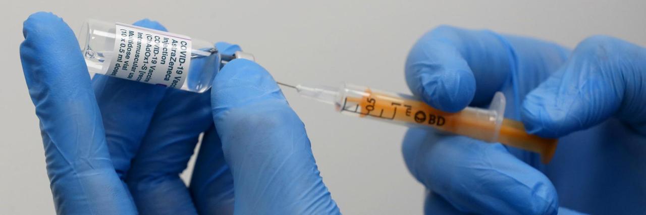 Zwei Hände in Handschuhen ziehen eine Spritze mit dem Astrazeneca-Impfstoff auf Zwei Hände in Handschuhen ziehen eine Spritze mit dem Astrazeneca-Impfstoff auf