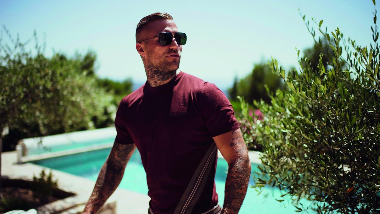 Der Rapper steht an einem Pool, trägt Sonnebrille und schaut zur Seite. Der Rapper steht an einem Pool, trägt Sonnebrille und schaut zur Seite.