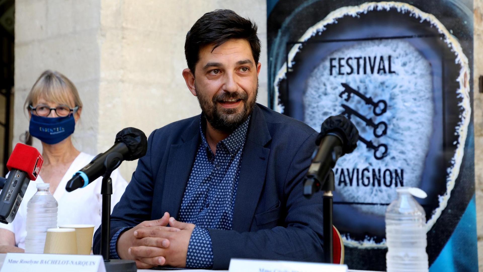 Festivalleiter Tiago Rodrigues sitzt im Sommeranzug vor Mikrofonen, hinter sich ein Schild des Theaterfestivals Avignon mit drei Schlüsseln. Festivalleiter Tiago Rodrigues sitzt im Sommeranzug vor Mikrofonen, hinter sich ein Schild des Theaterfestivals Avignon mit drei Schlüsseln.