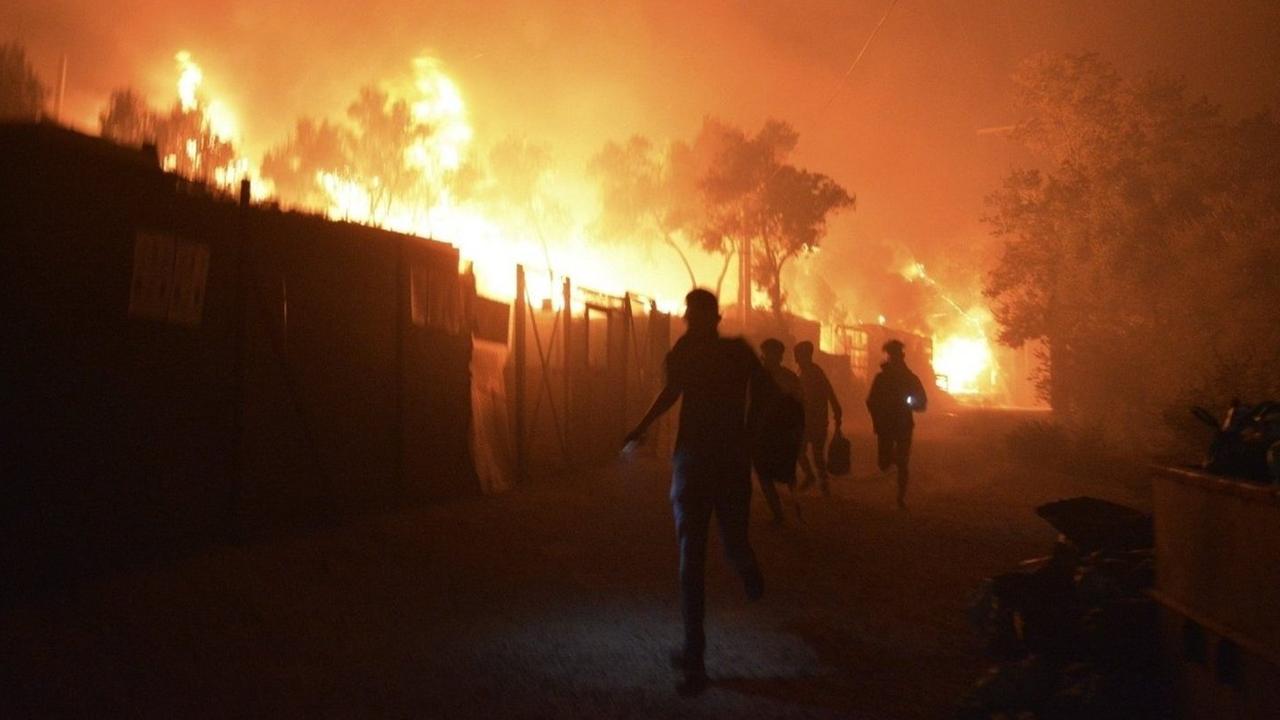 Man sieht die Flüchtenden als schwarze Silhouetten vor den hoch lodernden Feuern. Der Himmel ist rot gefärbt. Man sieht die Flüchtenden als schwarze Silhouetten vor den hoch lodernden Feuern. Der Himmel ist rot gefärbt.