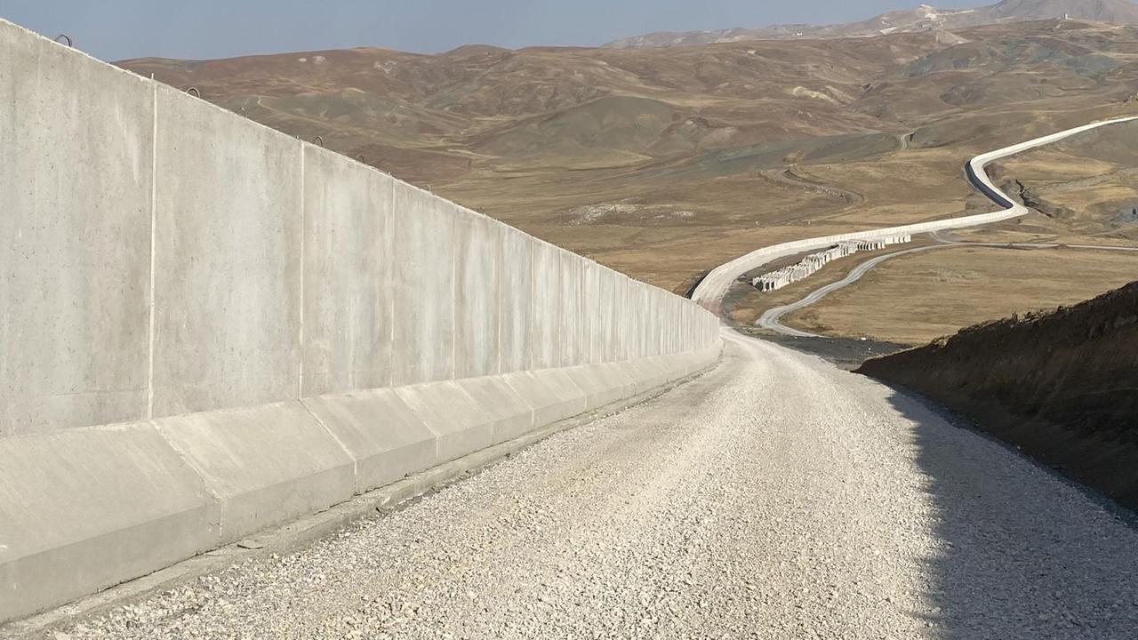 Eine lange Betonmauer schlängelt sich durch eine hügelige Landschaft. Eine lange Betonmauer schlängelt sich durch eine hügelige Landschaft.