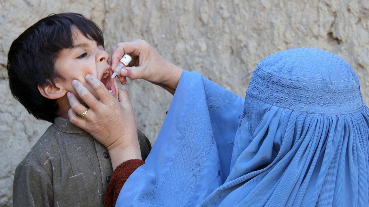 Eine Afghanin in blauer Burka tropf einem kleinen Jungen Polio-Impfstoff aus einem Fläschchen in den Mund.