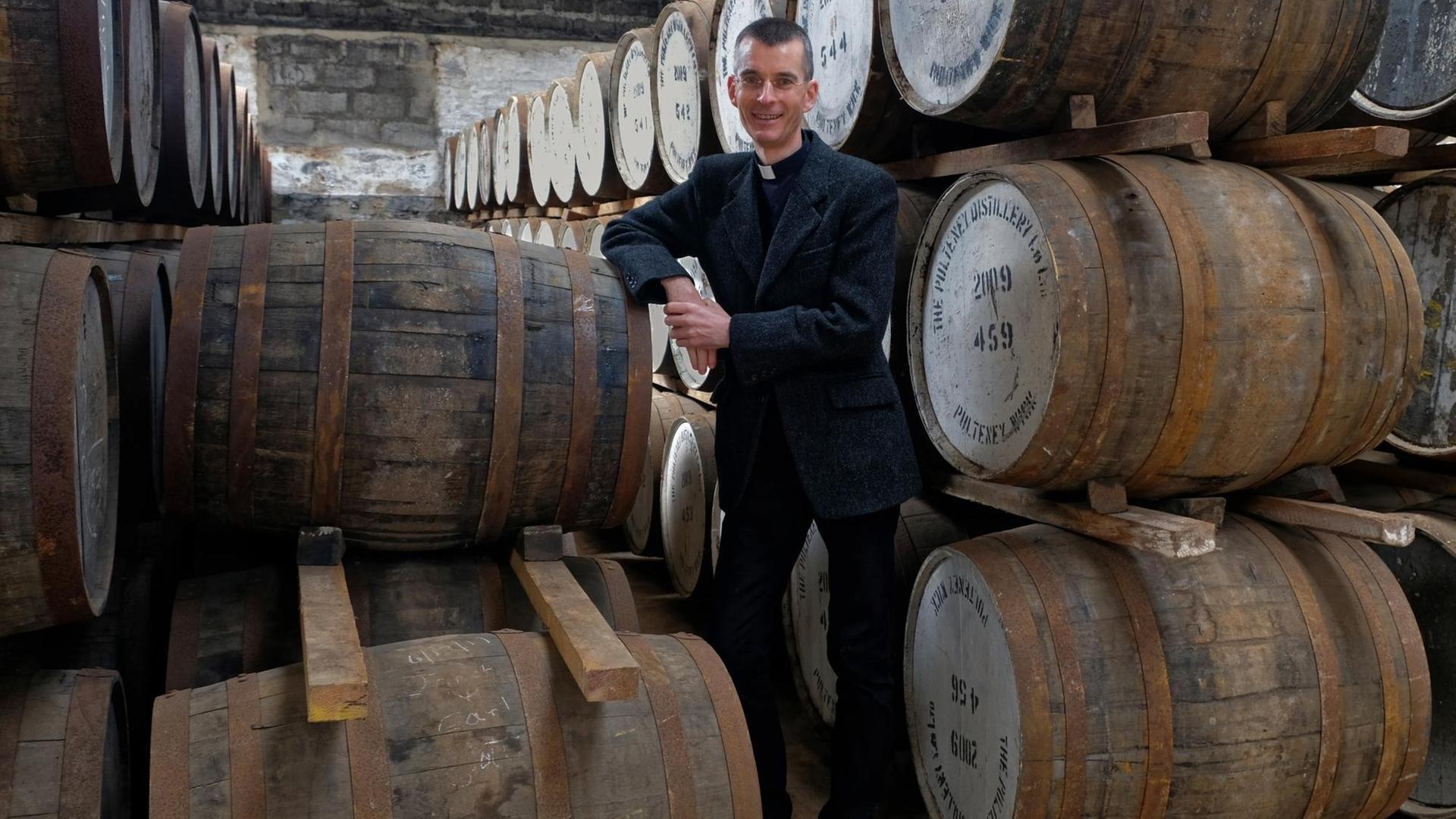 Pfarrer steht vor Whisky-Fässern Pfarrer steht vor Whisky-Fässern