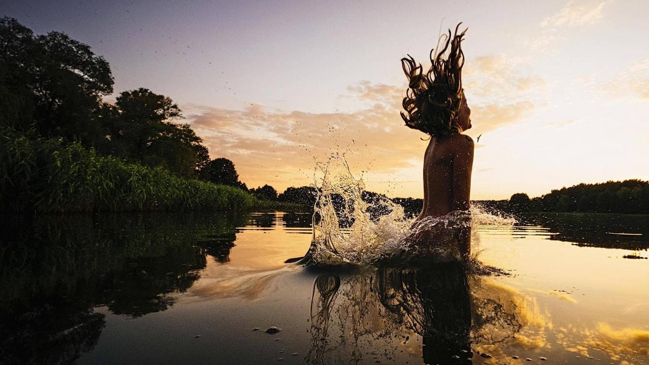 Ein Mädchen springt in einen See bei Sonnenuntergang, Mecklenburg-Vorpommern, Barnin.