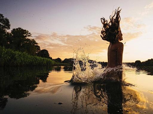 Ein Mädchen springt in einen See bei Sonnenuntergang, Mecklenburg-Vorpommern, Barnin.
