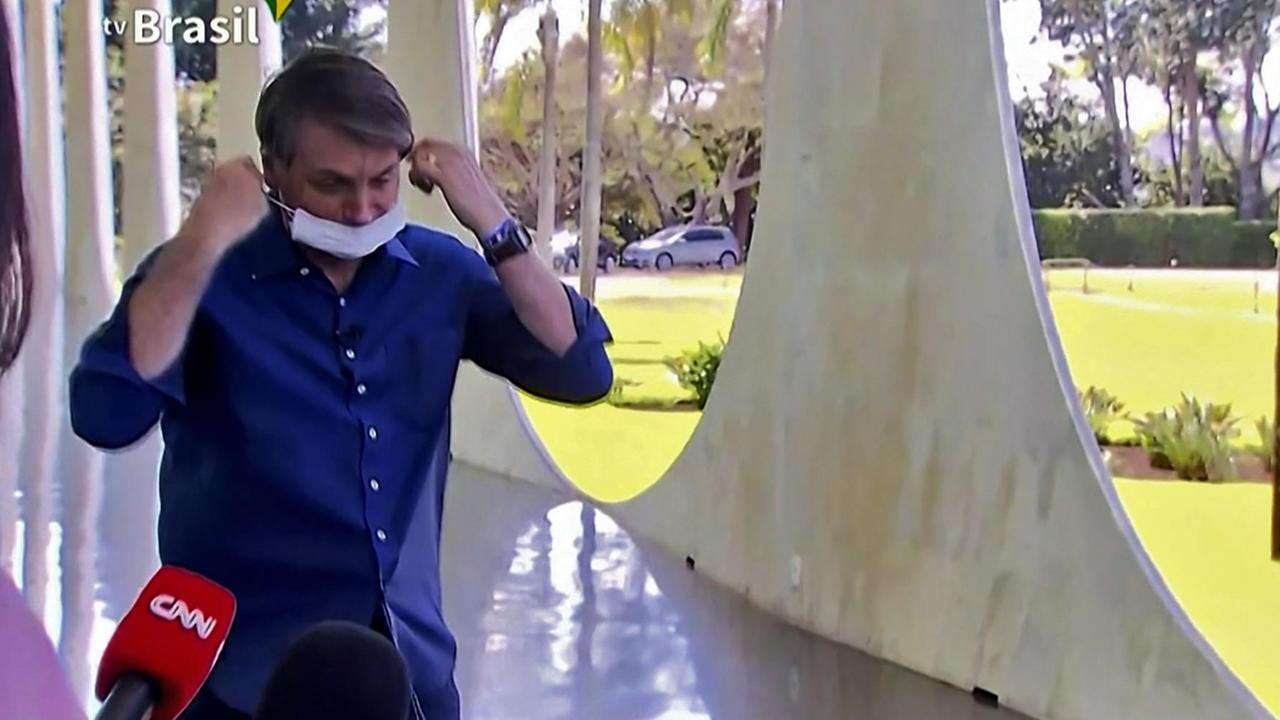 Brasiliens Präsident Bolsonaro hat eine Maske in den Händen, die bereits den Mund bedeckt - nicht jedoch die Nase. Brasiliens Präsident Bolsonaro hat eine Maske in den Händen, die bereits den Mund bedeckt - nicht jedoch die Nase.