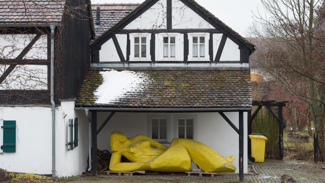 Eine gelbe Holzplastik liegt unter einem Vordach. Das sorbische Dorf lebt schon jetzt, was die Zukunft für weitere Orte in der Lausitz sein könnte.