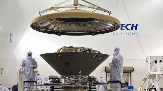 In the Astrotech facility technicians and engineers place the heatshield on the NASA Mars InSight Lander prior to encapsulation in its payload fairing at the Vandenberg Air Force Base Space Launch Complex 3 March 29, 2018 in Lompoc, California.