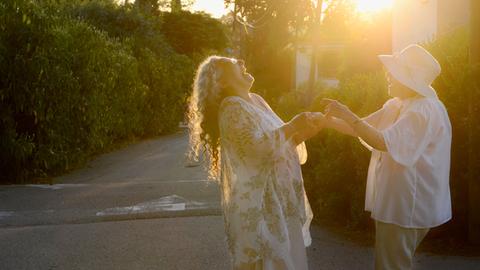 Zwei Frauen halten sich an den Händen und lachen, im Hintergrund die untergehende Sonne.