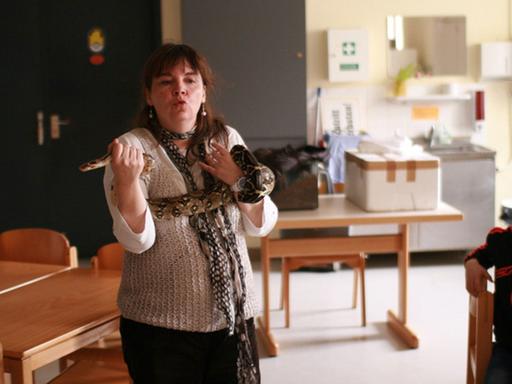 Eine Zoopädagogin trägt eine Schlange um den Körper geschlungen