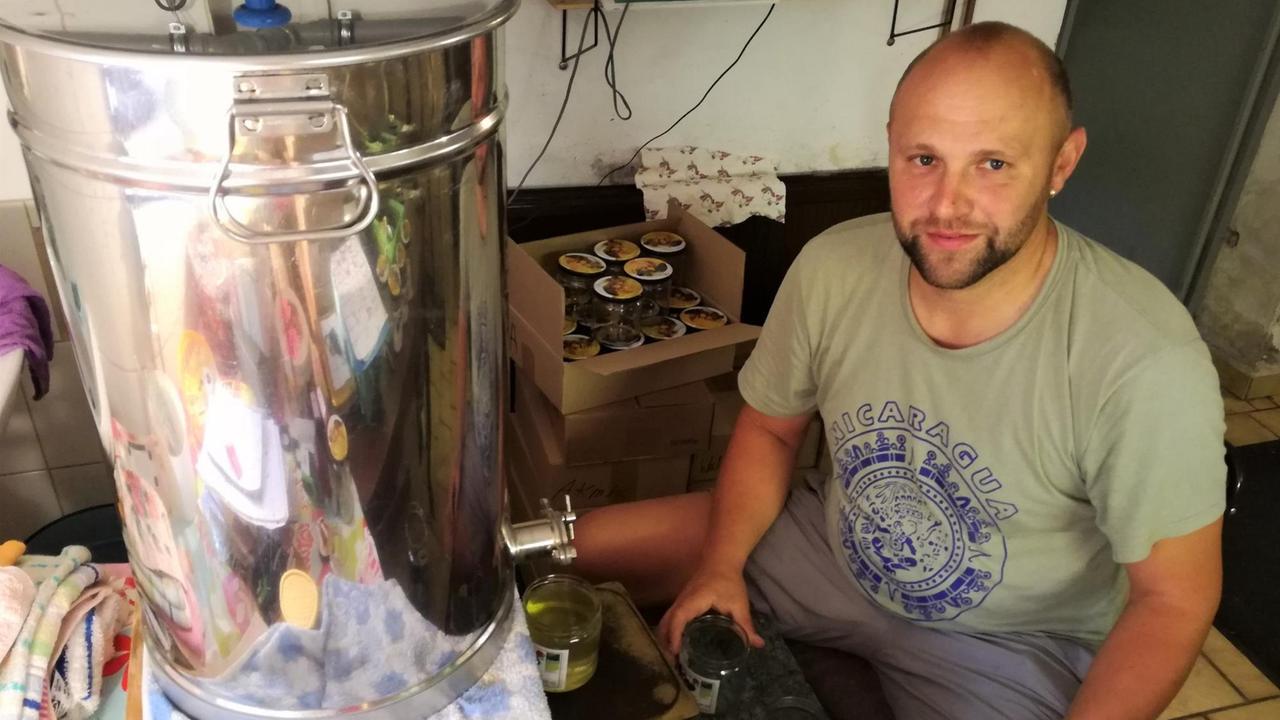 Mann im T-Shirt sitzt vor einem großen Edelstahlbehälter Mann im T-Shirt sitzt vor einem großen Edelstahlbehälter