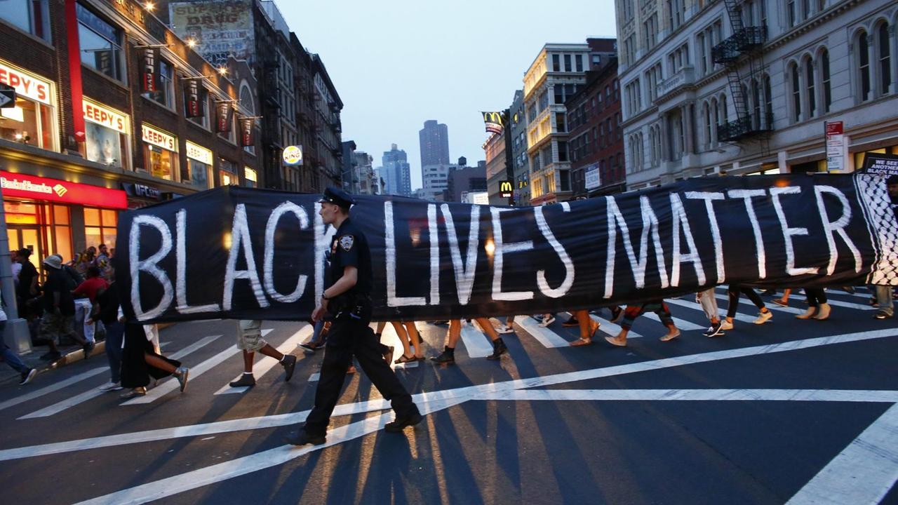 Bei einer Demonstration im Rahmen der "Black-lives-matter"-Bewegung in New York geht ein Polizist vor einem Transparent. Bei einer Demonstration im Rahmen der "Black-lives-matter"-Bewegung in New York geht ein Polizist vor einem Transparent.