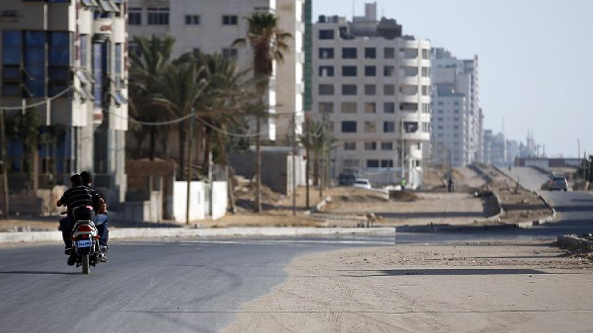Palästinenser fahren mit einem Motorrad entlang einer ausgestorbenen Straße im Gaza-Streifen.