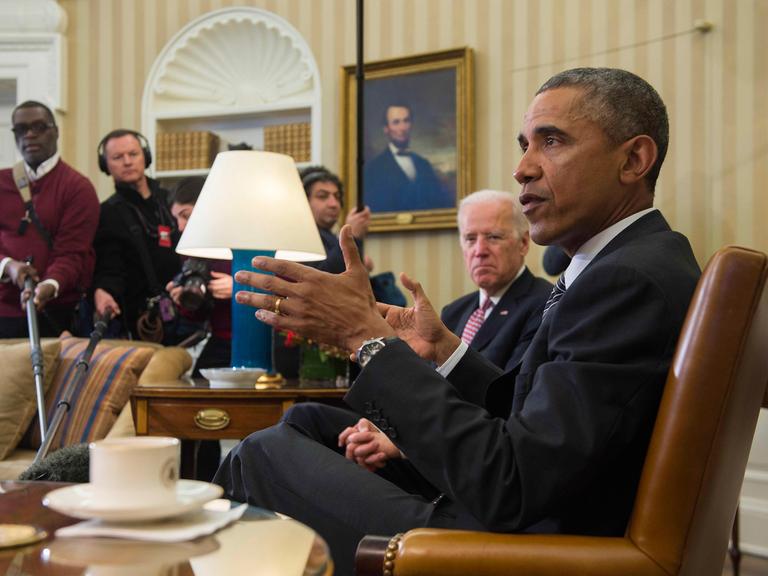US-Präsident Barack Obama und sein Vize Joe Biden sitzen vor Presse im Oval Office, Obama im Vordergrund, von der Seite aufgenommen.