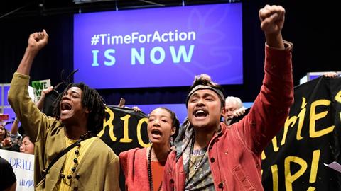 Junge Klimaaktivisten, zum Teil mit hochgestreckten Händen, auf der UN-Klimakonferenz in Madrid. Im Hintergrund ist der Hashtag "TimeForAction, IS NOW" zu sehen.