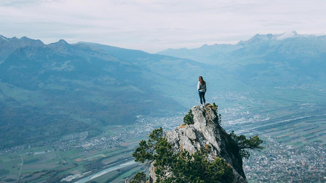 Eine junge Frau steht in Liechtenstein auf dem Fürstensteig und blickt auf die Landschaft unter ihr.