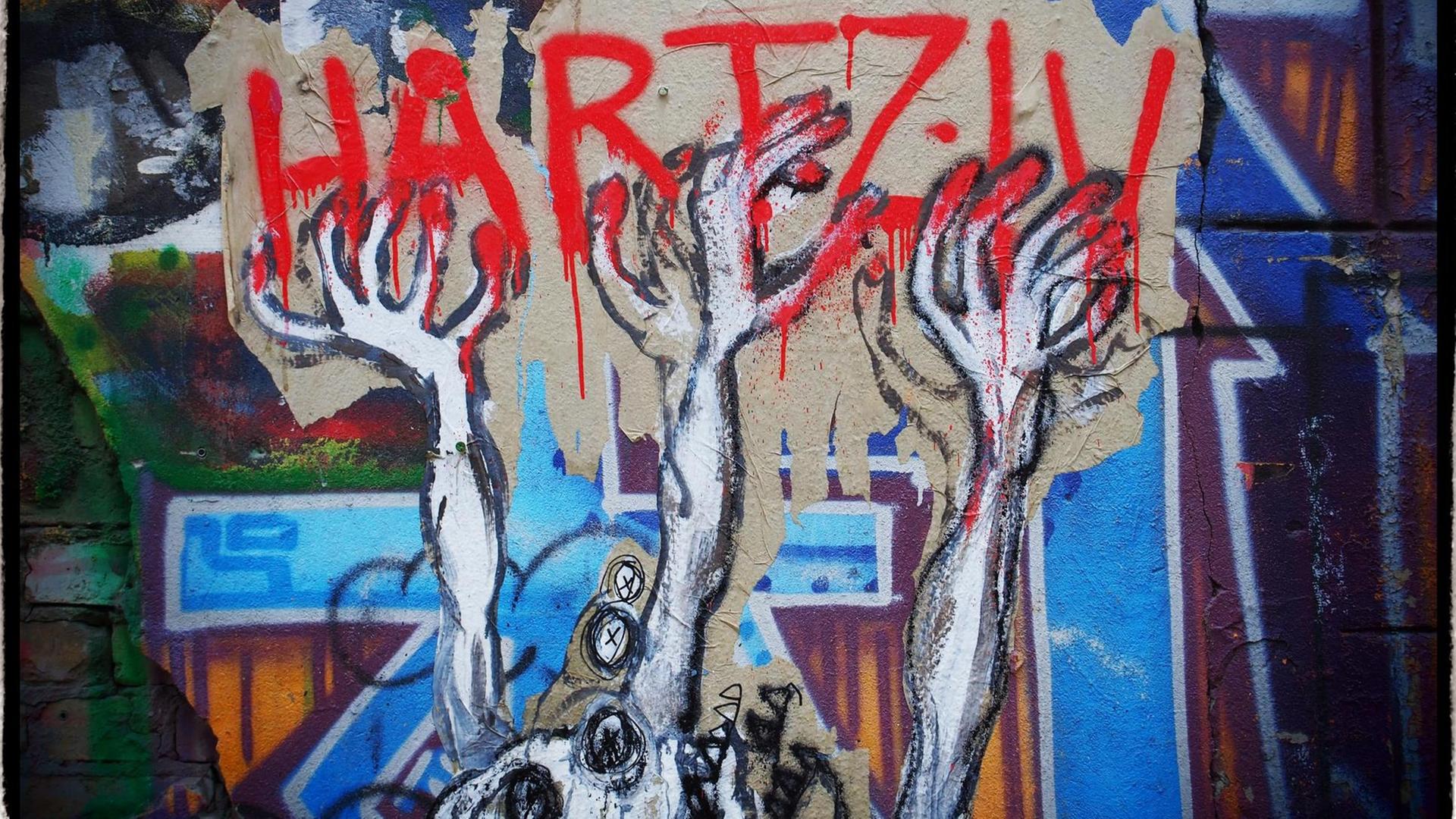 Ein unbekannter Street-Art-Künstler hat auf einer Mauer an einem besetzten Haus in Berlin im Bezirk Mitte dieses Bild geschaffen, das seine Meinung zu den Hartz IV Gesetzen drastisch wiedergibt: Verzwifelte HÄnde greifen nach dem roten Schriftzug Hartz IV, im Hintergrund sind Grabkreuze zu sehen. Ein unbekannter Street-Art-Künstler hat auf einer Mauer an einem besetzten Haus in Berlin im Bezirk Mitte dieses Bild geschaffen, das seine Meinung zu den Hartz IV Gesetzen drastisch wiedergibt: Verzwifelte HÄnde greifen nach dem roten Schriftzug Hartz IV, im Hintergrund sind Grabkreuze zu sehen.