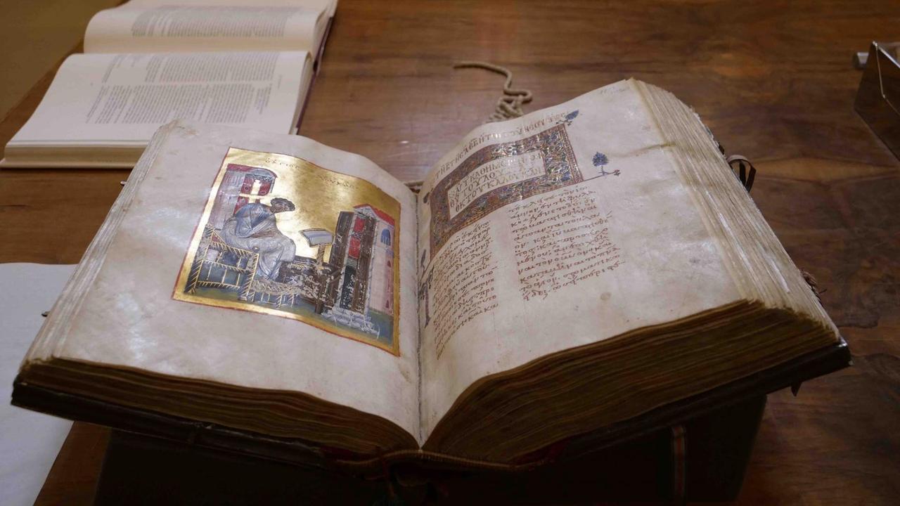 Ein aufgeschlagenes dickes Buch mit leicht angegilbten Seiten zeigt auf der linken Seite eine Illustration mit goldenem Hintergrund, auf der eine Andachtsfigur zu sehen ist. Ein aufgeschlagenes dickes Buch mit leicht angegilbten Seiten zeigt auf der linken Seite eine Illustration mit goldenem Hintergrund, auf der eine Andachtsfigur zu sehen ist.