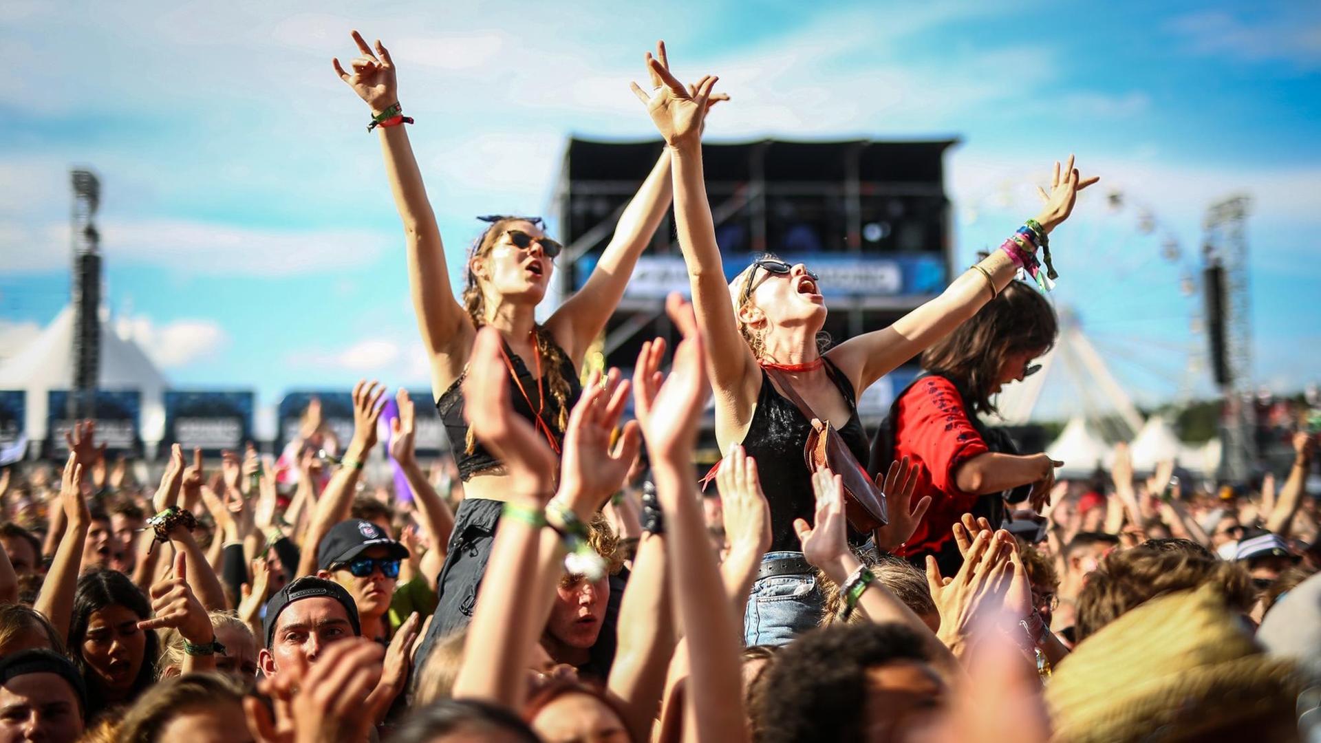 Das Bild zeigt die Menge des Southside Festival mit den Armen in die Luft gestreckt. Zwei Frauen stechen dabei besonders heraus: sie sitzen mit ausgebreiteten Armen auf den Schultern von zwei anderen Personen und singen zur Musik des Konzerts mit. Das Bild zeigt die Menge des Southside Festival mit den Armen in die Luft gestreckt. Zwei Frauen stechen dabei besonders heraus: sie sitzen mit ausgebreiteten Armen auf den Schultern von zwei anderen Personen und singen zur Musik des Konzerts mit.