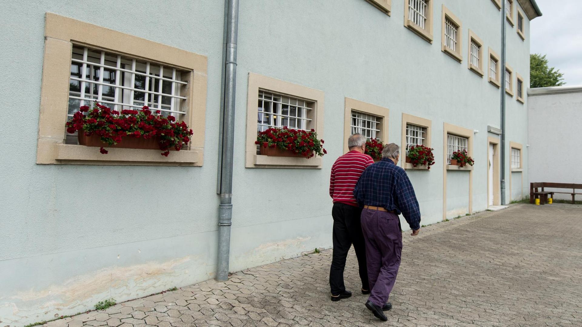 Zwei Insassen der Justizvollzugsanstalt Singen (Baden-Württemberg) laufen am 27.07.2017 im Innenhof des Gefängnisses an vergitterten Fenstern vorbei. Beide sind Senioren. Es ist bundesweit das einzige Gefängnis für Senioren.
