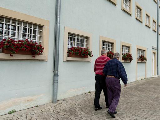 Zwei Insassen der Justizvollzugsanstalt Singen (Baden-Württemberg) laufen am 27.07.2017 im Innenhof des Gefängnisses an vergitterten Fenstern vorbei. Beide sind Senioren. Es ist bundesweit das einzige Gefängnis für Senioren.