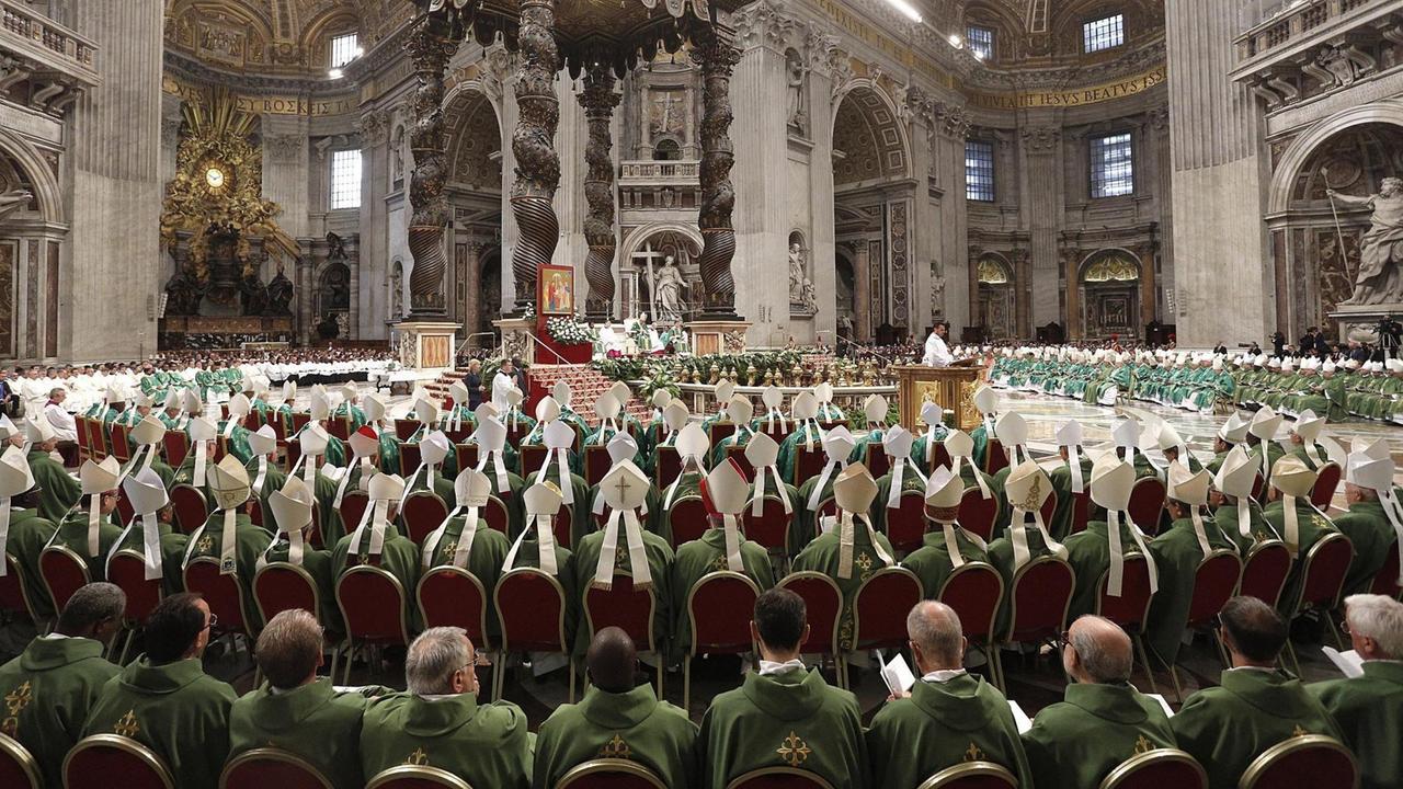 Die Bischöfe sitzen in grünen Gewändern im Dom in Petersdom.