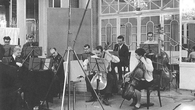 Schwarz-weiß Foto: Die Musiker tragen schwarze Anzüge mit Schlips, die Cellistin Rock mit Bluse und einer weißen Strickjacke. Mikrofonstative stehen vor dem Ensemble.