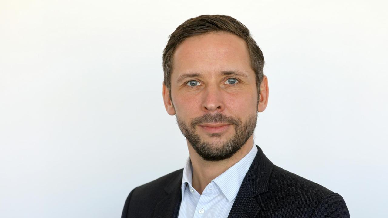 Tobias Woitendorf blickt in die Kamera, er trägt ein dunkles Sakko und ein helles Hemd ohne Krawatte. Er hat einen Vollbart, Tobias Woitendorf blickt in die Kamera, er trägt ein dunkles Sakko und ein helles Hemd ohne Krawatte. Er hat einen Vollbart,