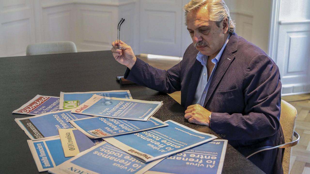 Alberto Fernández sitzt an einem Tisch mit Zeitungen vor sich, die mit Schlagzeilen zum Coronavirus aufmachen. Alberto Fernández sitzt an einem Tisch mit Zeitungen vor sich, die mit Schlagzeilen zum Coronavirus aufmachen.