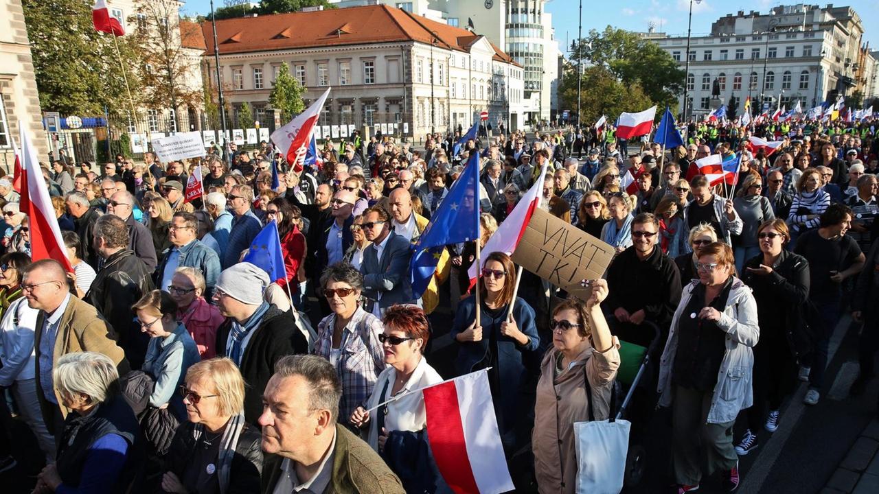 Eine große Menschenmenge mit Transparenten und polnischen Fahnen zieht eine Straße entlang. Dahinter sieht man mehrere Gebäude. Eine große Menschenmenge mit Transparenten und polnischen Fahnen zieht eine Straße entlang. Dahinter sieht man mehrere Gebäude.