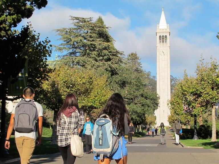Studenten gehen über den Campus der Universität in Berkeley mit dem Campanile, einem Glockenturm und Wahrzeichen des Gebäudes.