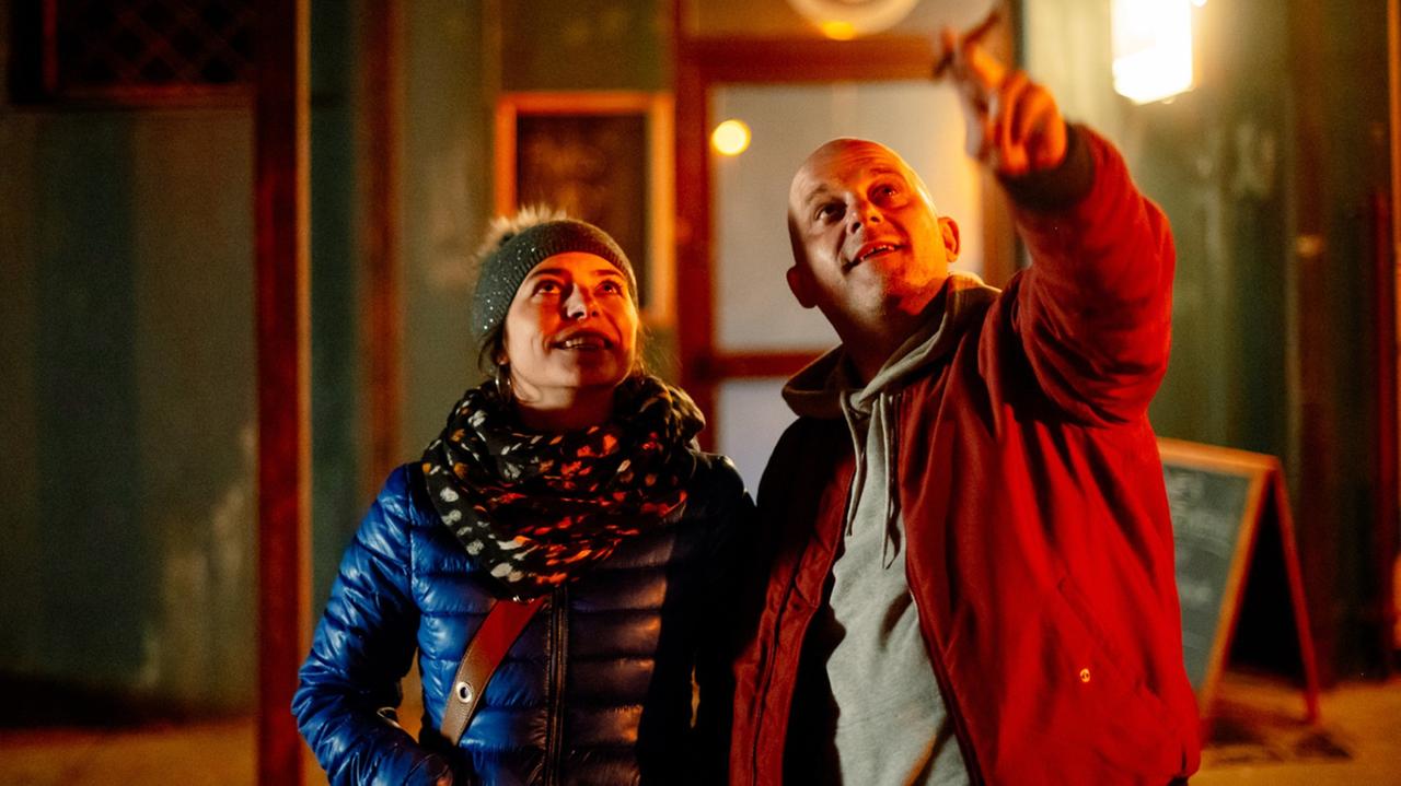 Ein bulliger Mann und eine Frau stehen auf der Straße und blicken nach oben. Ein bulliger Mann und eine Frau stehen auf der Straße und blicken nach oben.