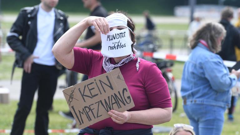 Eine Teilnehmerin einer Demonstrationen gegen die Anti-Corona-Maßnahmen der Politik steht auf der Theresienwiese in München und hält ein Schild mit der Aufschrift "Kein Impfzwang" in der Hand. Auf ihrem Mundschutz steht "Mundtot und rechtlos". 