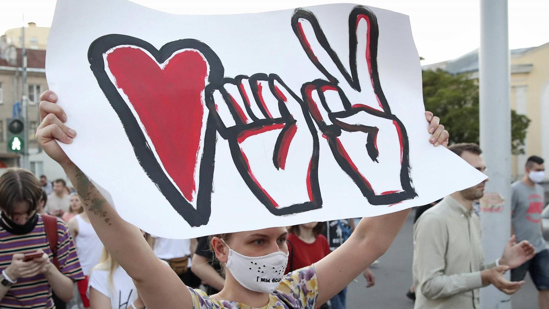 Teilnehmerin einer Demonstration in Minsk mit einem Plakat, das die drei Symbole der Bewegung darstellt: Eine Faust, ein Herz und ein Victory-Zeichen. Teilnehmerin einer Demonstration in Minsk mit einem Plakat, das die drei Symbole der Bewegung darstellt: Eine Faust, ein Herz und ein Victory-Zeichen.