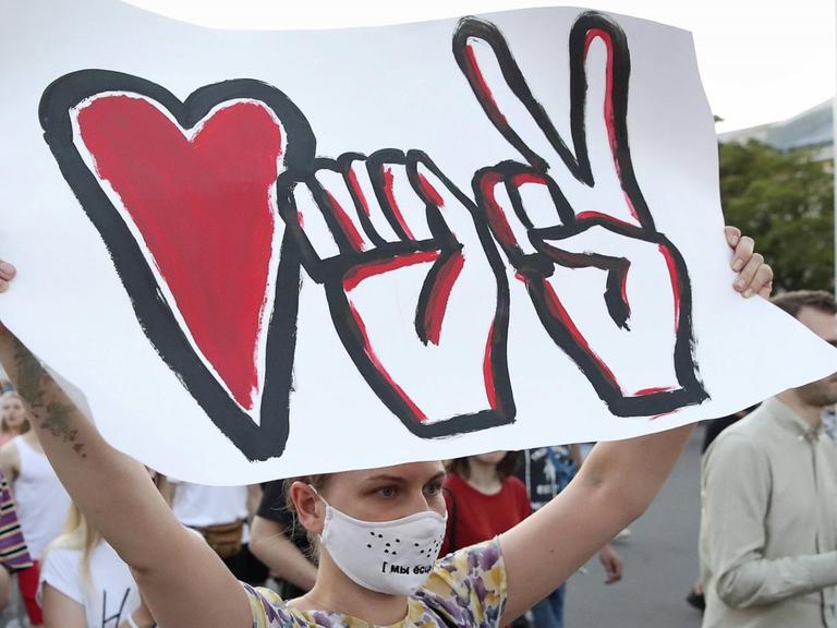 Teilnehmerin einer Demonstration in Minsk mit einem Plakat, das die drei Symbole der Bewegung darstellt: Eine Faust, ein Herz und ein Victory-Zeichen.