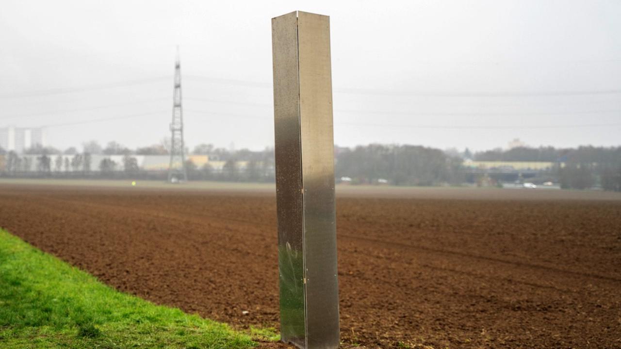 Ein Monolith aus Metall steht auf einem Feld. Ein Monolith aus Metall steht auf einem Feld.