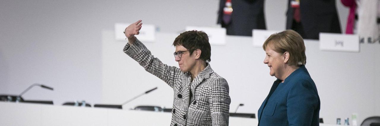 Annegret Kramp-Karrenbauer winkt ins Publikum, rechts neben ihr steht Angela Merkel in lockerer Pose Annegret Kramp-Karrenbauer winkt ins Publikum, rechts neben ihr steht Angela Merkel in lockerer Pose