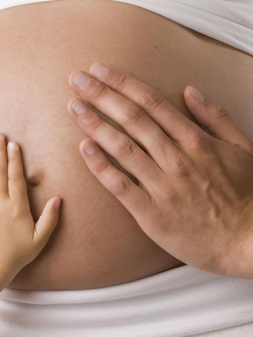 Zwei Hände berühren den Bauch einer Schwangeren.