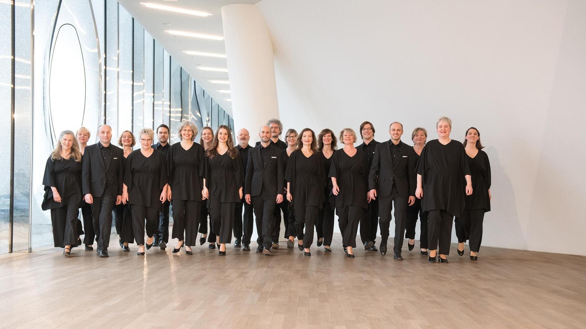 Eine Gruppe von schwarz gekleideten Sängerinnen und Sängern steht halb vor einer Glasfassade, halb vor einer weißen Wand. Im Jahr 2018 posierte der NDR Chor in der Hamburger Elbphilharmonie. Eine Gruppe von schwarz gekleideten Sängerinnen und Sängern steht halb vor einer Glasfassade, halb vor einer weißen Wand. Im Jahr 2018 posierte der NDR Chor in der Hamburger Elbphilharmonie.