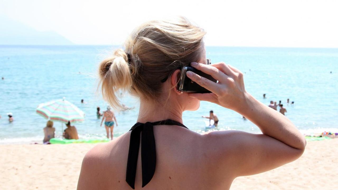 Eine Frau telefoniert mit ihrem Mobiltelefon am Strand. Eine Frau telefoniert mit ihrem Mobiltelefon am Strand.