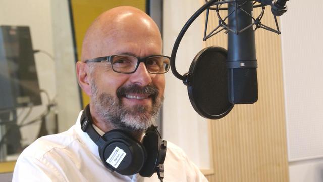 Christoph Maria Herbst im DLF-Studio 2019 vor dem Mikrofon und mit Kopfhörern um den Hals